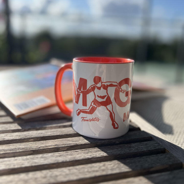 Tennisletics An image of a bright red Magical Moments mug sat next to a book on a wooden table.